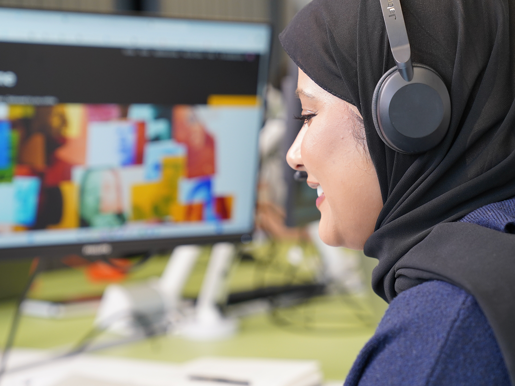 A woman working with black headphones looking at computer screen