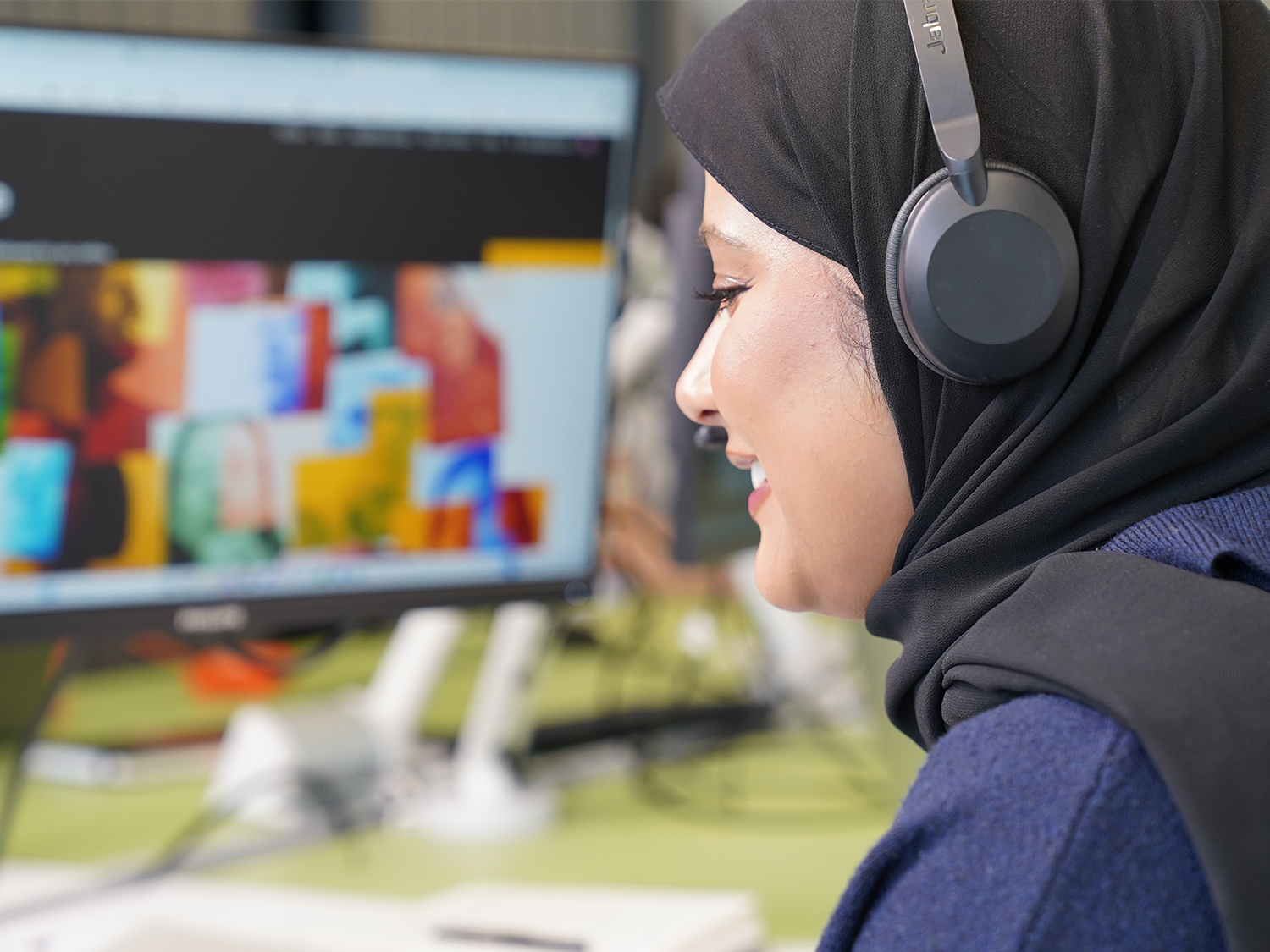 A woman working with black headphones looking at computer screen