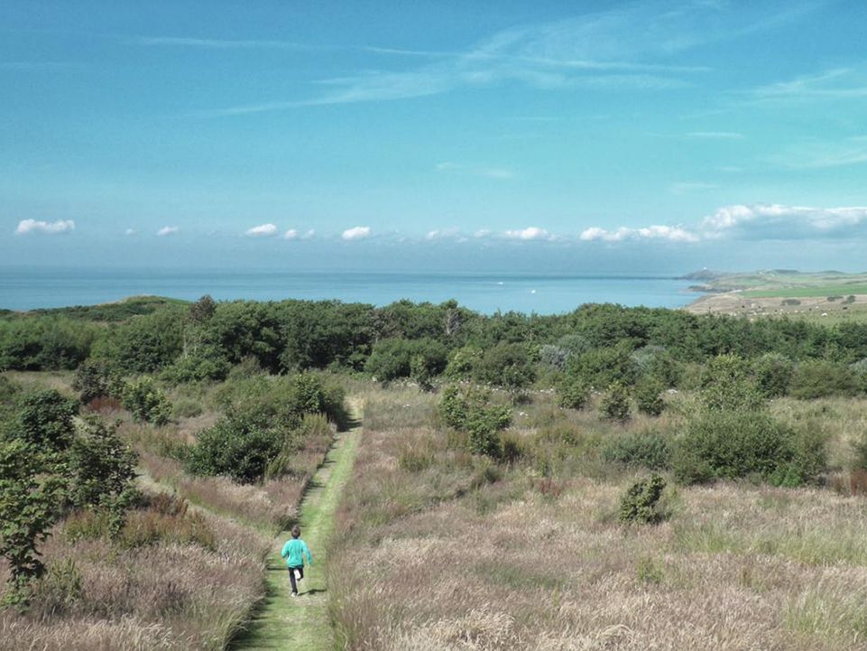 Wide-angle shot of a woman running on a coastal path.