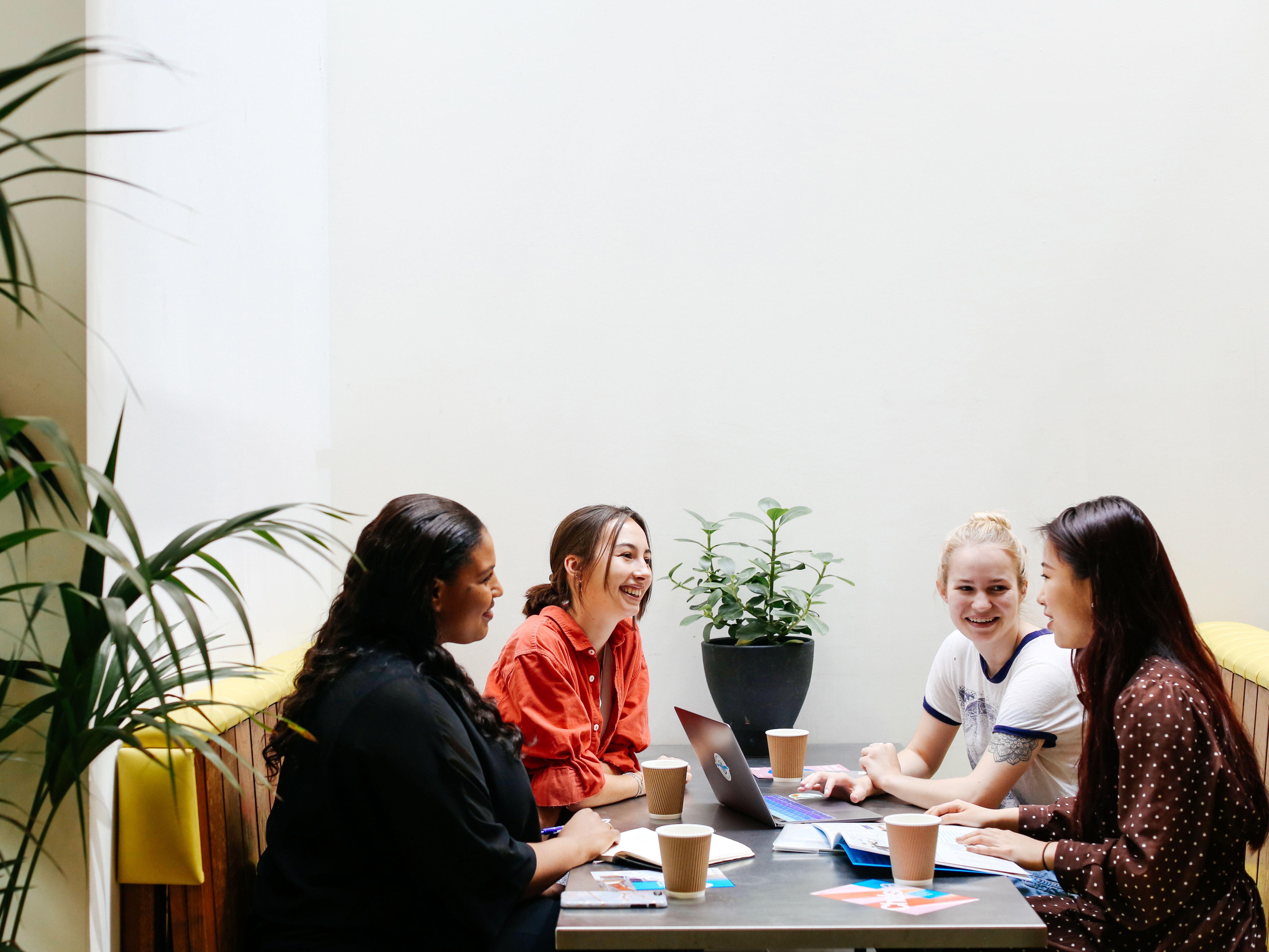 4 students sit in a booth at a canteen, they are chatting and laughing.
