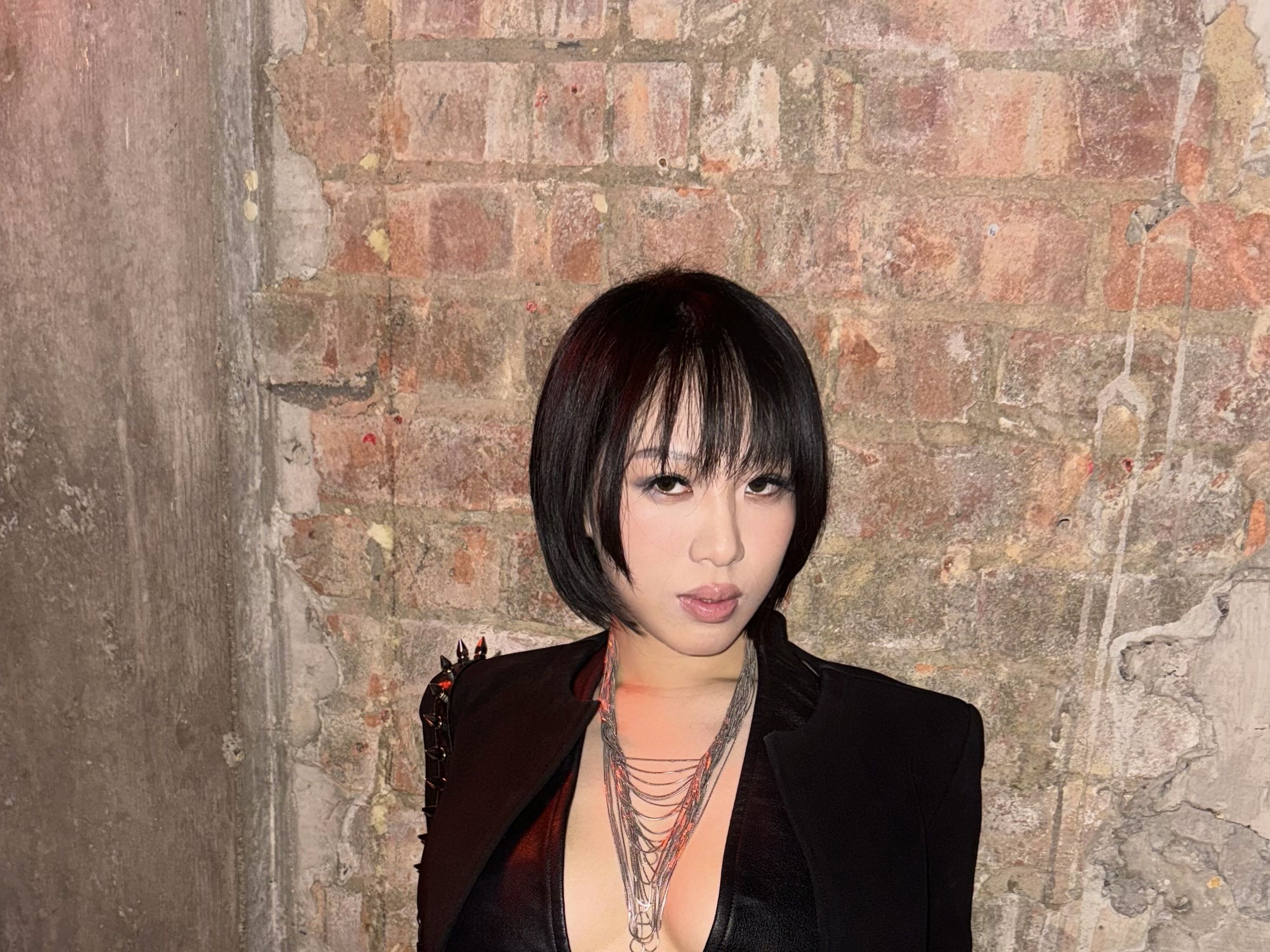 Lancy Liu, standing in front of a concrete wall, wearing a black suit blazer and crop top