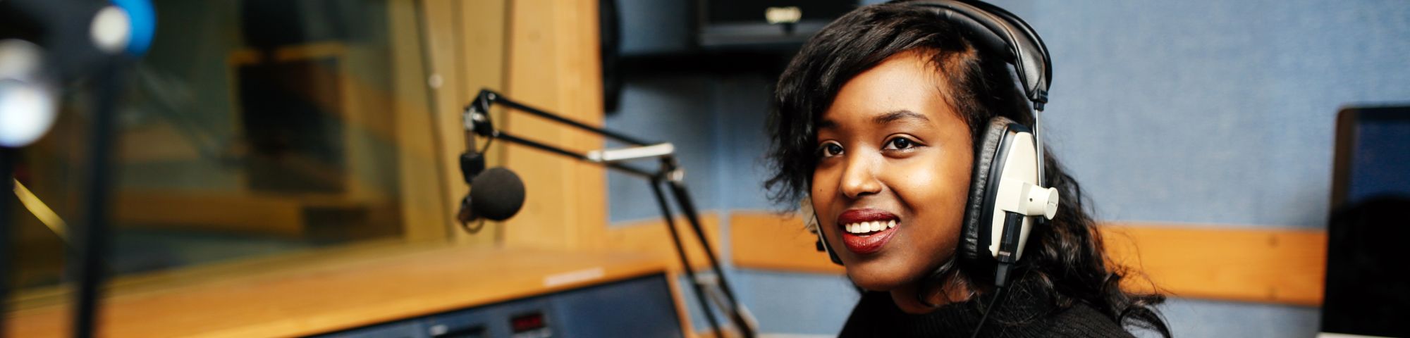 Woman in a radio booth with headphones on and a multicoloured jumper