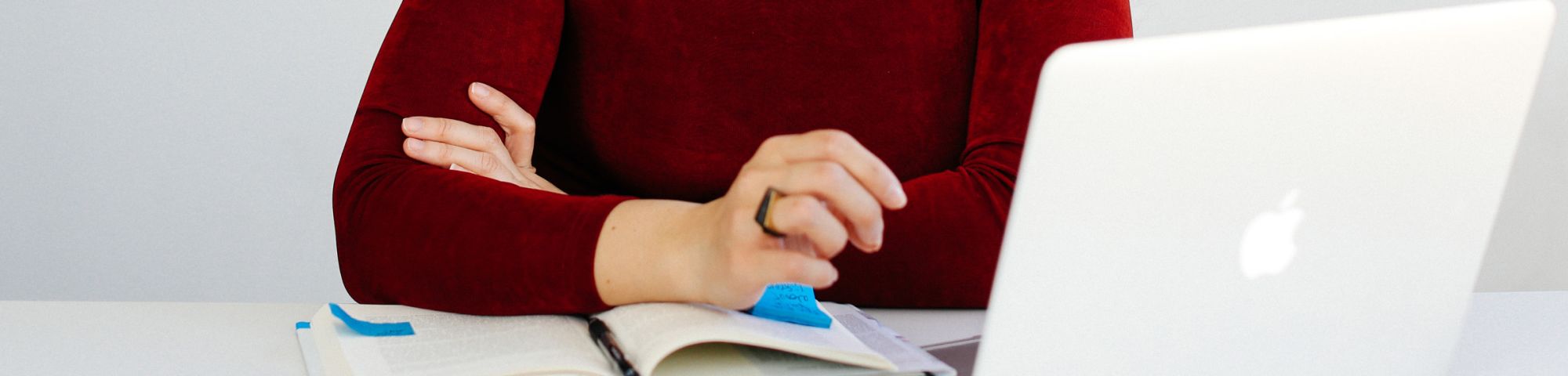 Close up shot of someone with folder arms on a desk with books, papers and a computer