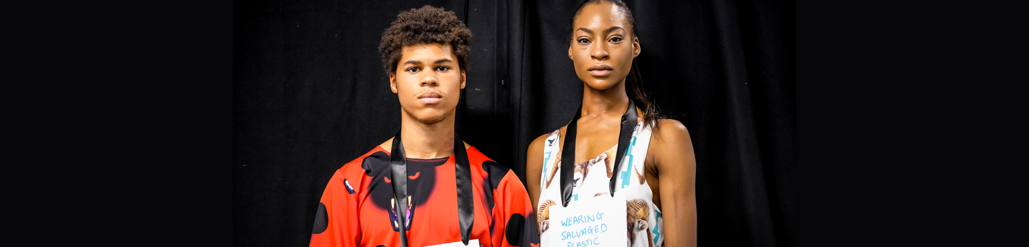 Two models wearing signs saying 'wearing salvaged plastic' from Vin+Omi's LFW presentation