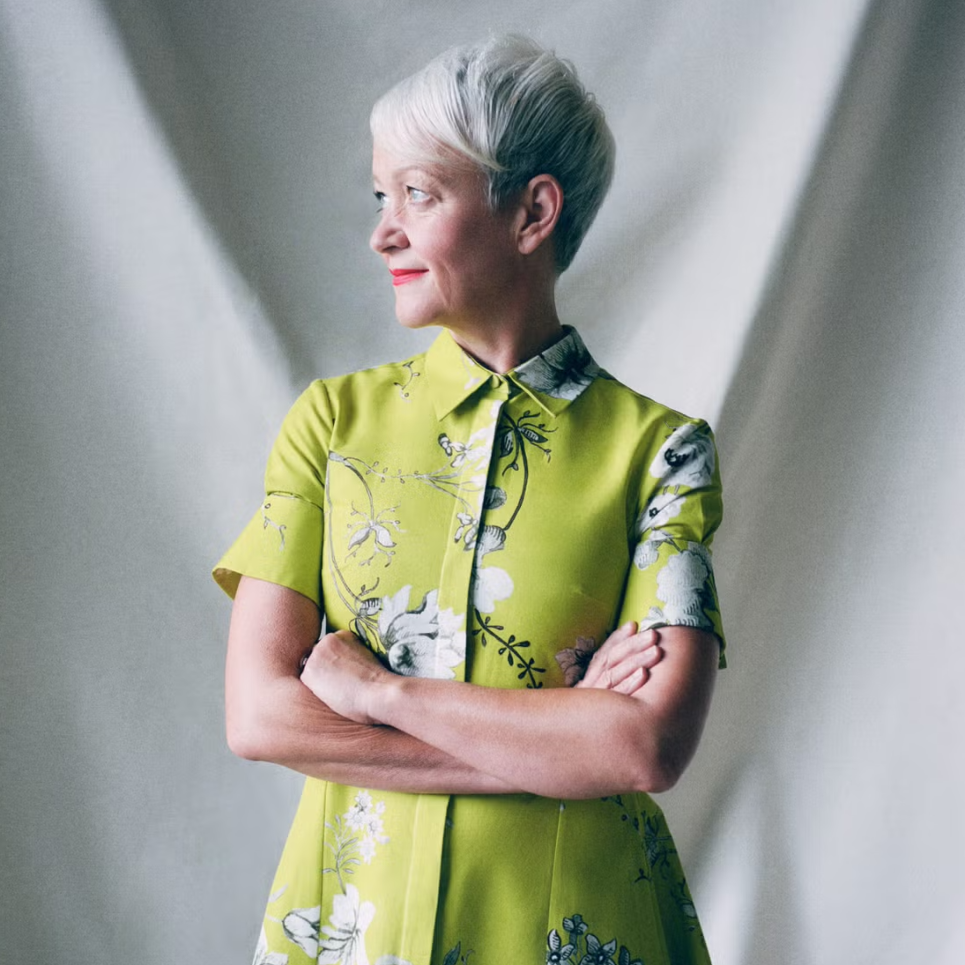 Maria stands looking to the side, in a bright green floral dress.