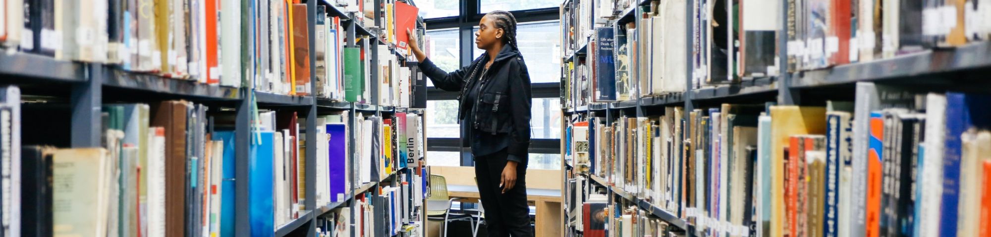 Student standing on a stool in the middle of two bookshelves.