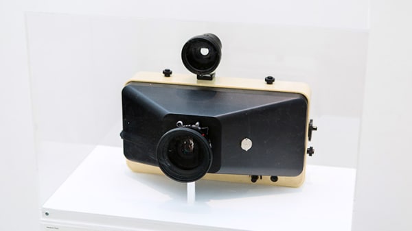 A vintage camera enclosed in a transparent box atop a plinth.