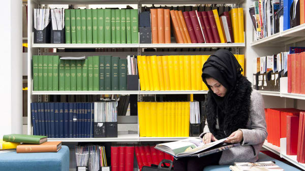 Photo of a woman sitting in between some book shelves reading a book