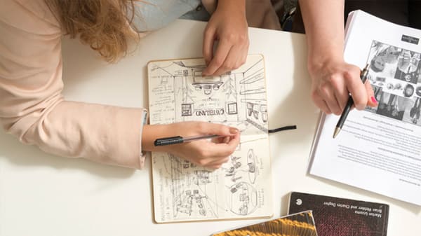 Photo of a pair of hands drawing in a sketch book using a pen