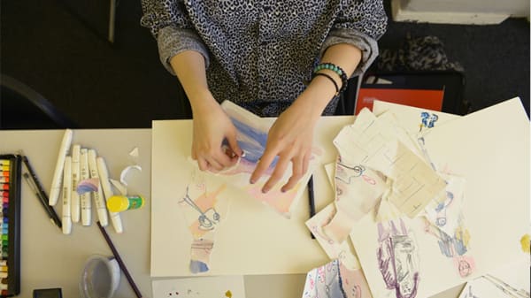 Photo taken from above of a pair of hands working with pieces of paper with drawings on them