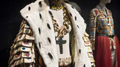 Image of a manequin with a large crucafix around its neck and a fur collar