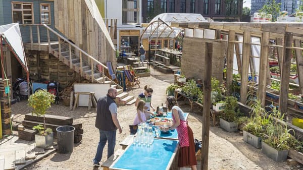 An open allotment with a trestle table down with middle and people are serving drinks and food.