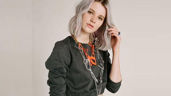 Photo of a woman wearing a grey jumper with a large orange necklace