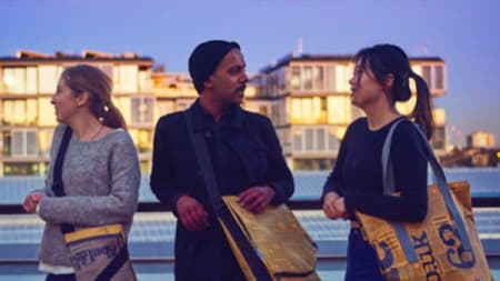 Three people of a rooftop wearing bags created from recycled packaging