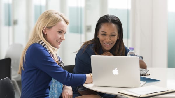 A photograph of two students smiling and looking at a laptop screen.