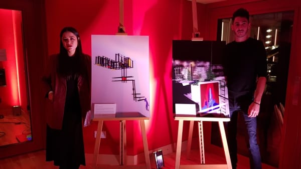 Two people stood next to canvases in a room light with a red light