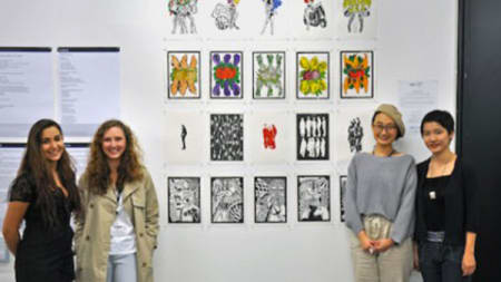 Four women stood either side of a collection of illustrations displayed on a wall