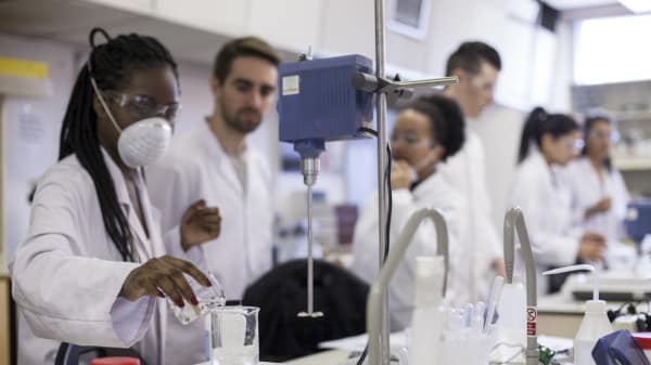 Cosmetic Science students from London College of Fashion in a lab.In the foreground a person is pouring clear liquid into a glass beaker.