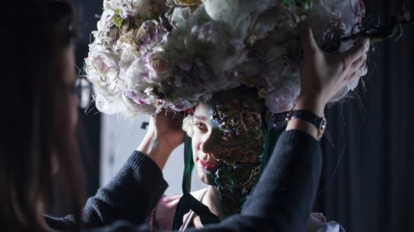 A model having a large floral headpiece adjusted on her head