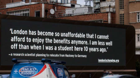 A large black billboard with white writing on it above a busy road