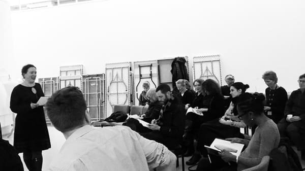 Black and white photo of woman standing in front of group of people sitting down