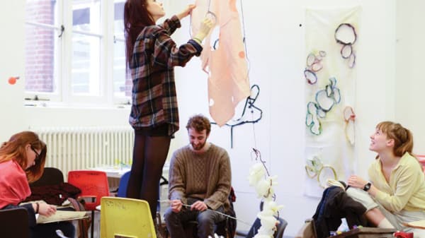 Photo of a girl standing on a chair hanging a piece of orange material with three others sitting on chairs around her