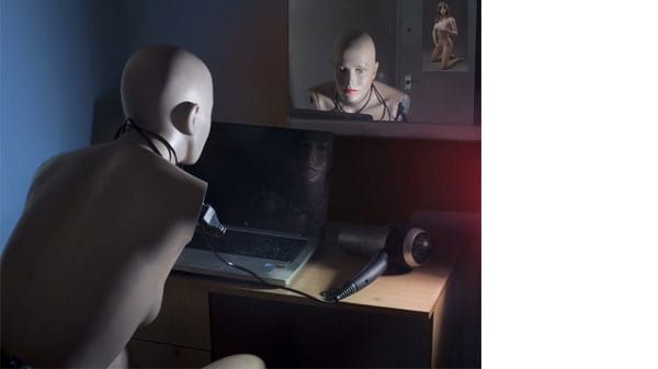 A mannequin looking at a laptop reflected in a mirror