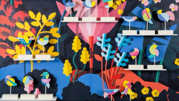 Miniature bird statues in front of a very colourful painted background of plants and trees