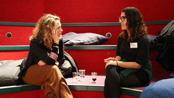 Photograph of an Industry Mentoring Scheme event at London College of Communication. Mentors and mentees having a discussion in a red seating space.