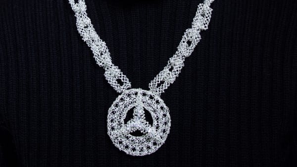 Silver metal woven into a necklace which has a Mercedes Benz logo pendant