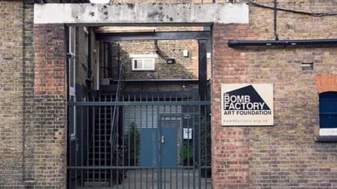 A brick building, a sign next to the door says 'Bomb Factory Art Foundation'