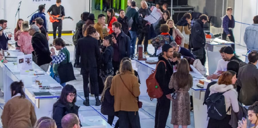 people mull around tables looking at work from graduating students