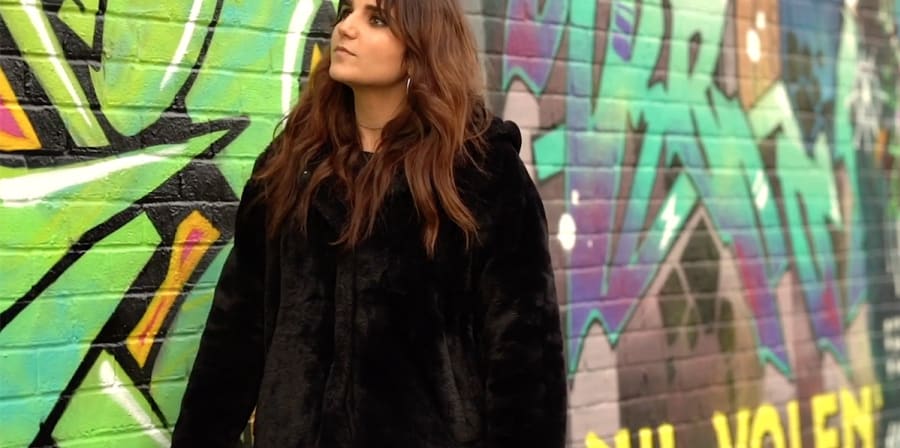 Revital stands in front of a heavily graffiti-ed brick wall.