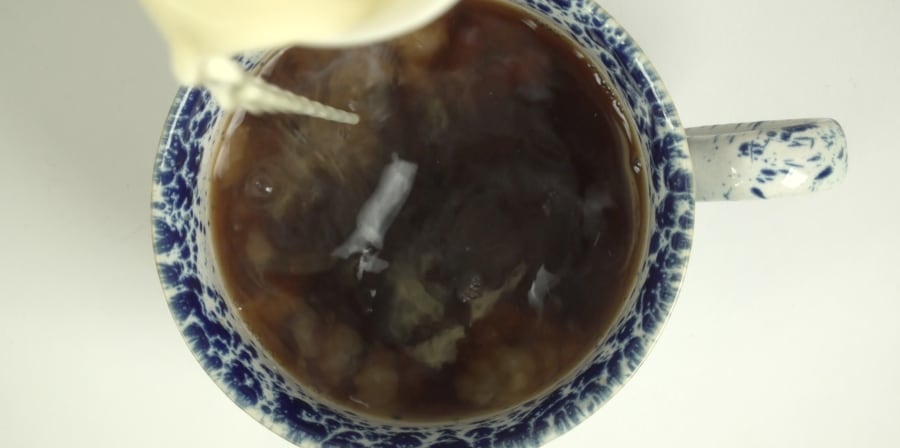 A still of milk being poured into a teacup.