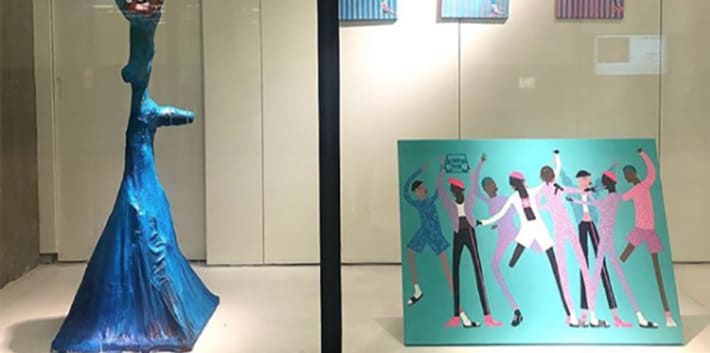 Photograph of a blue sculpture and paintings of illustrated people dancing on display in the Window Gallery at Central Saint Martins
