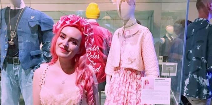 Young project team volunteer Ellie Medhurst in pink standing in front of mannequin dressed in her clothes donated to Queer Looks exhibition, Brighton Museum, 2018-19.