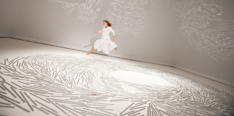 A person running around a room in a white dress. The floor of the room is covered in white marks.