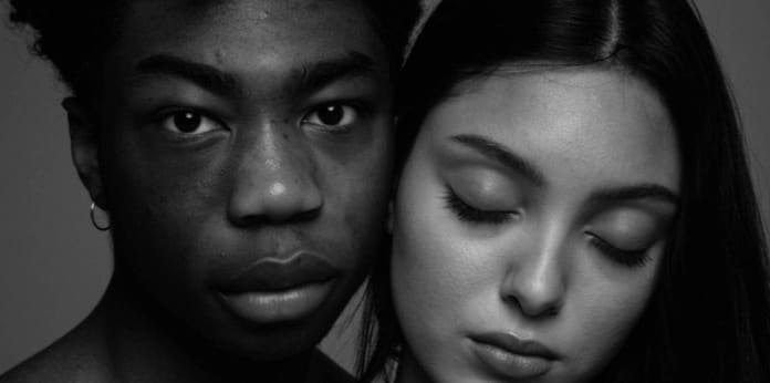 A black and white photograph of two models, one of whom has closed their eyes.