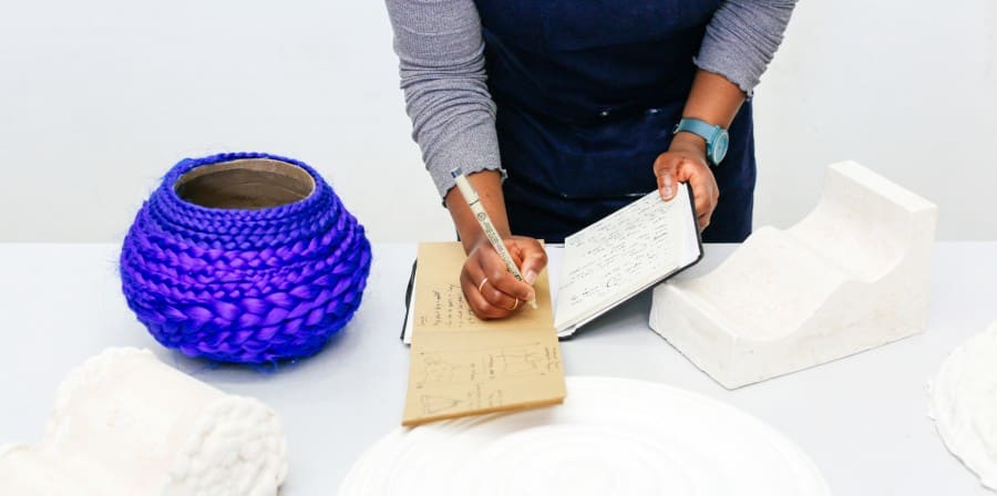Student writing in a notebook with her sculptures