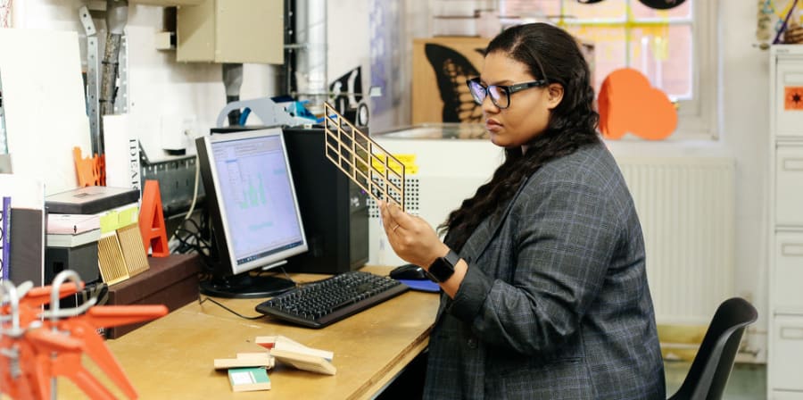 Woman looking at 3D printing and sitting at a desk.