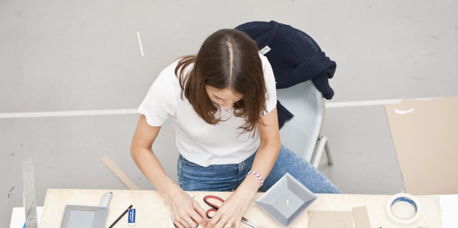 View down to a student seated at a desk and using various tool and cardboard materials.
