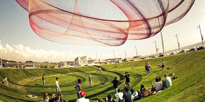 Photo of a group of people standing on the grass under a large piece of red and orange material