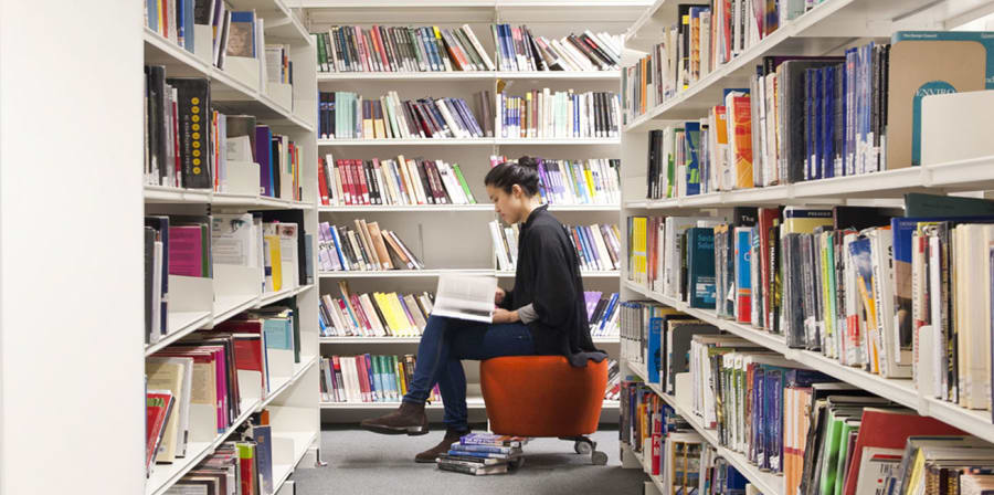 Photo of a girl sat in between two book shelves reading