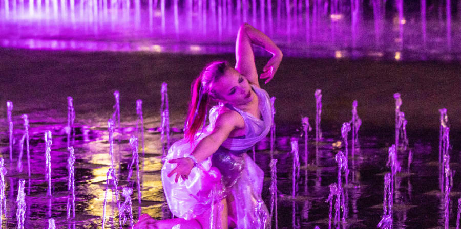 a girl dances in a costume amongst the fountains outside of csm
