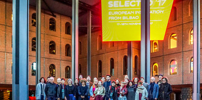Image of students and staff standing on a brightly lit stage as part of a Graduate School student funded event.