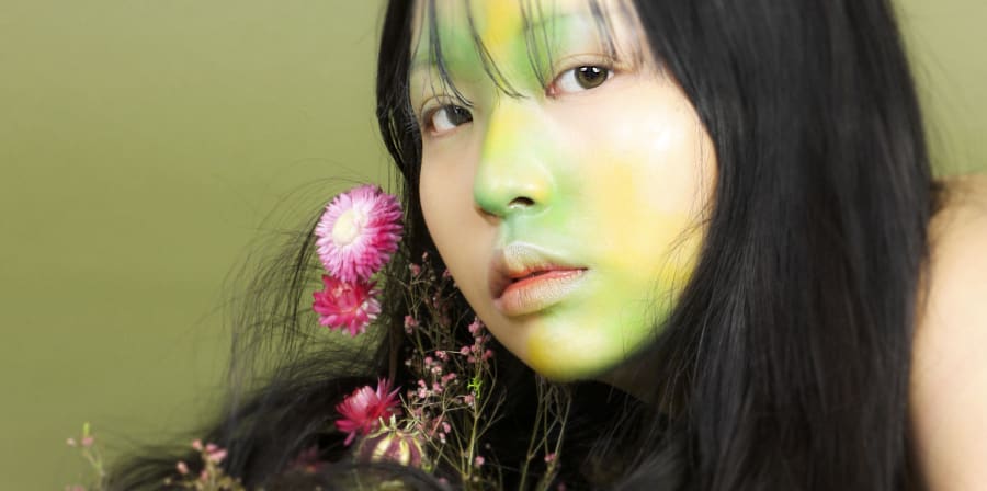 A girl with green paint on her face against a green backdrop