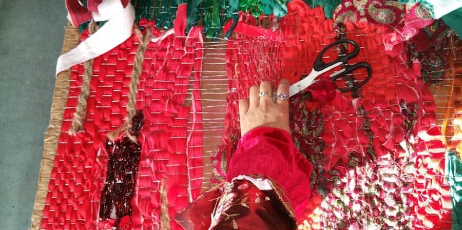 birds eye view of hand holding a pair of scissors a piece of weaving lies underneath