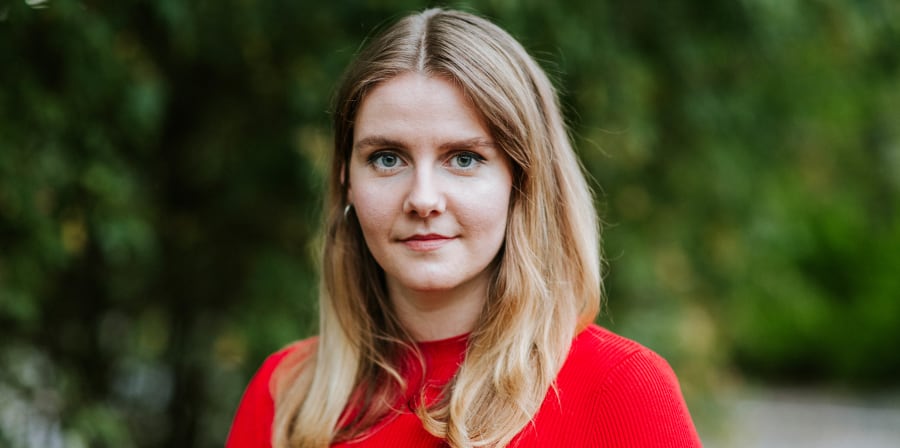 Woman in red standing in front of tree.