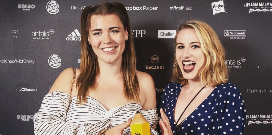 Amy and Georgina smile with their yellow pencil award.