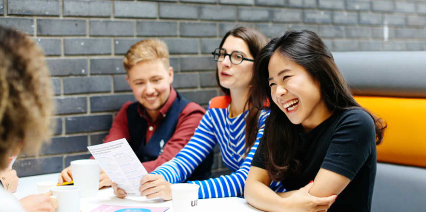One asian female student laughing, sitting with three other students in a booth with books and papers on table